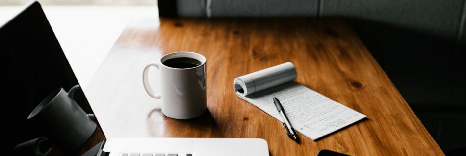 MacBook Pro, white ceramic mug,and black smartphone on table