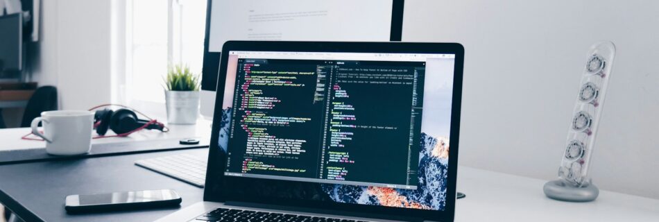 A MacBook with lines of code on its screen on a busy desk