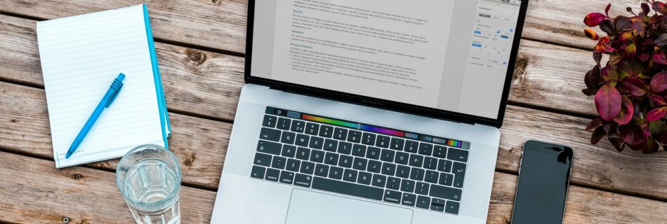 silver MacBook beside space gray iPhone 6 and clear drinking glass on brown wooden top