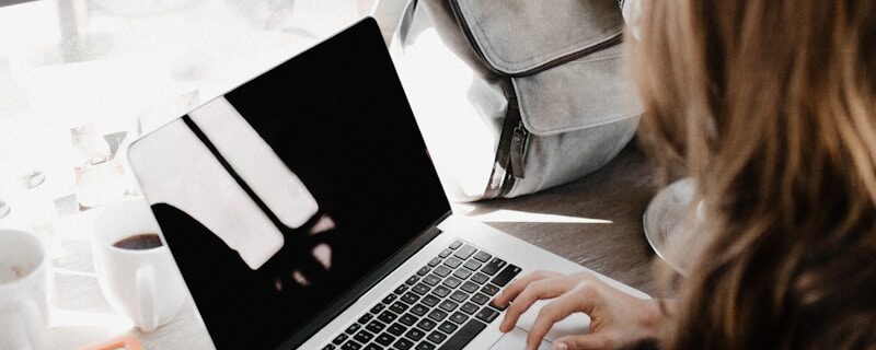 girl wearing grey long-sleeved shirt using MacBook Pro on brown wooden table